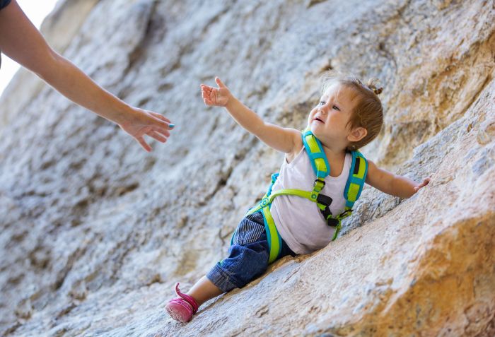 Little girl in climbing gear stretching out hand