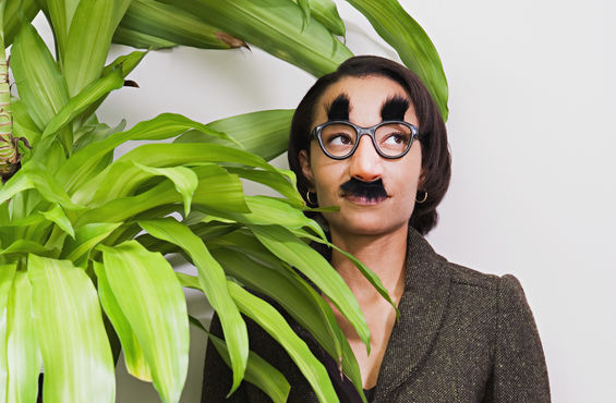 Businesswoman hiding behind plant wearing disguise