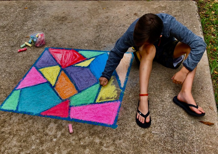 kid drawing chalk art on sidewalk